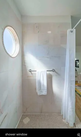 Shower enclosure featuring a circular window with tile surround, large format wall tiles, mosaic tile flooring, and a chrome towel bar