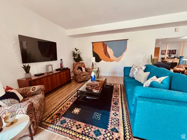 Spacious living area featuring wood-finish flooring, white wall finishes, and an open entryway to an additional room