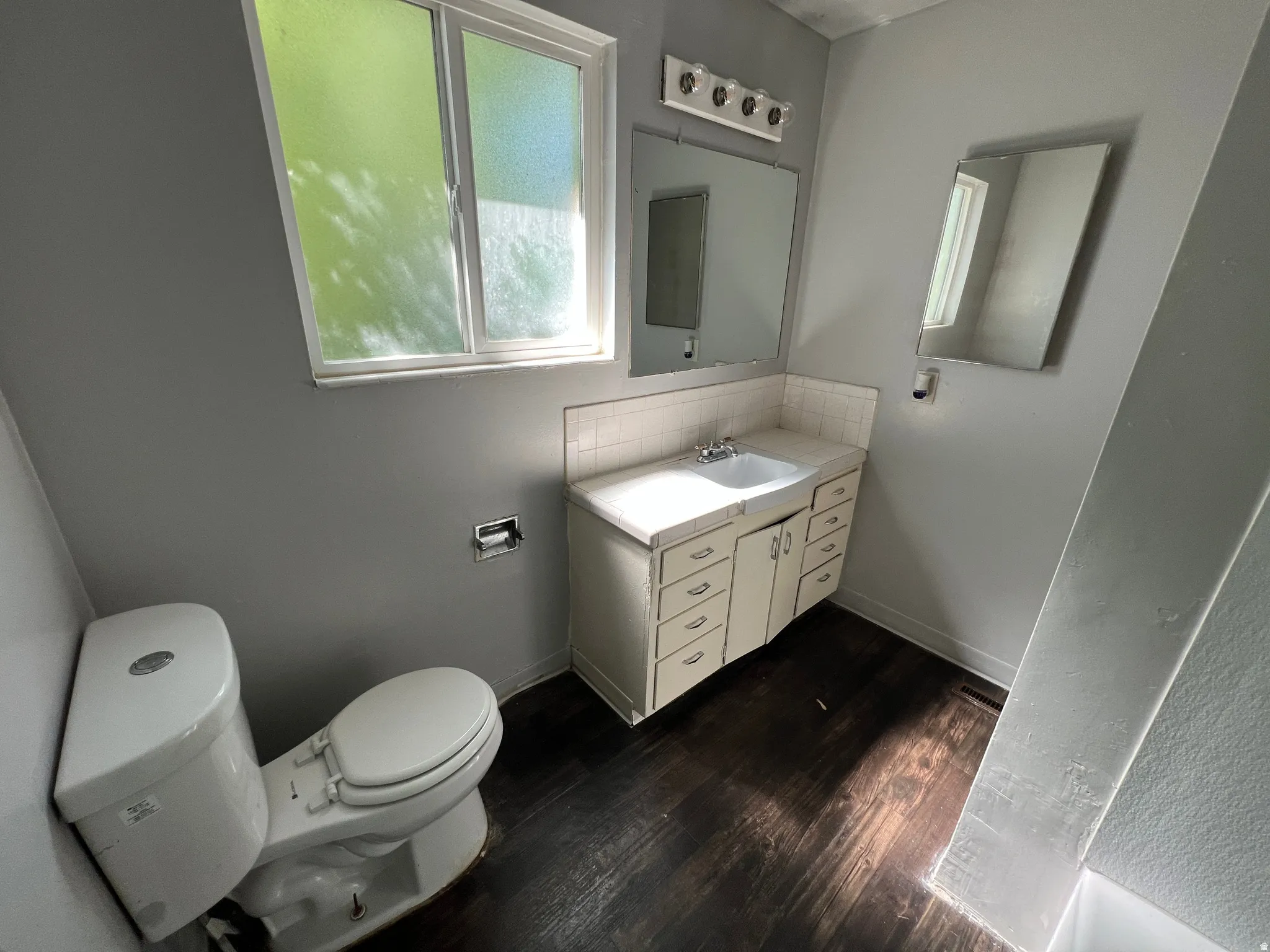Bathroom featuring a white vanity with integrated sink, a rectangular mirror, and wood-finish flooring