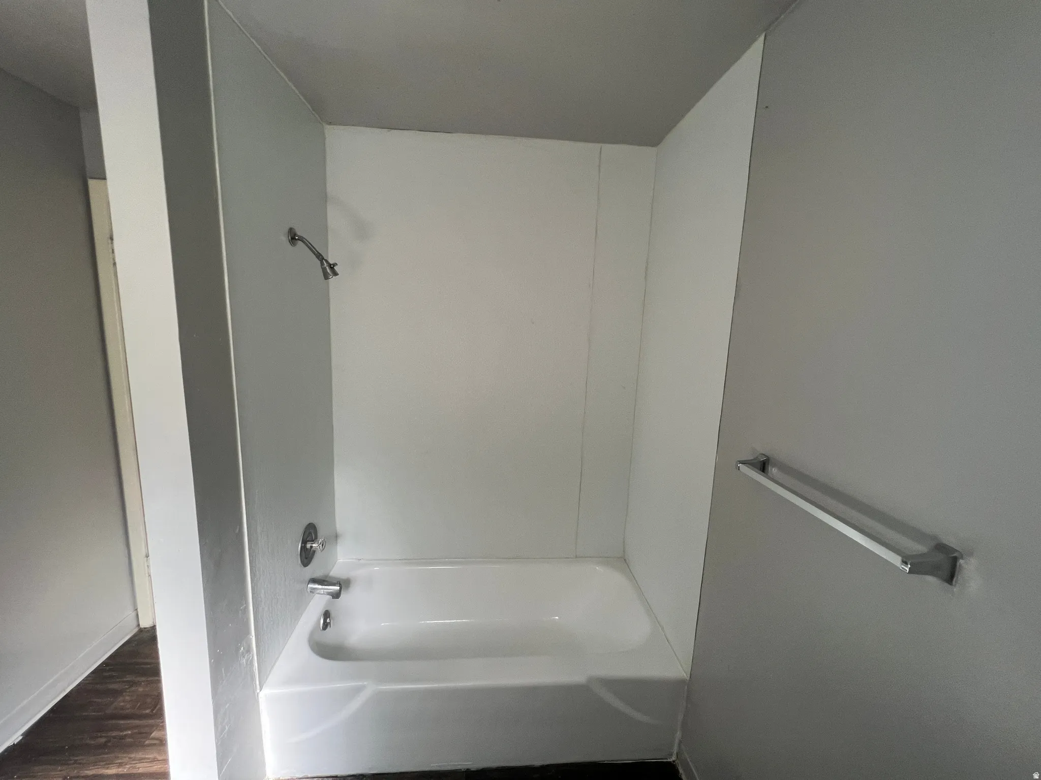 White bathtub and shower surround with chrome fixtures, set against light gray walls