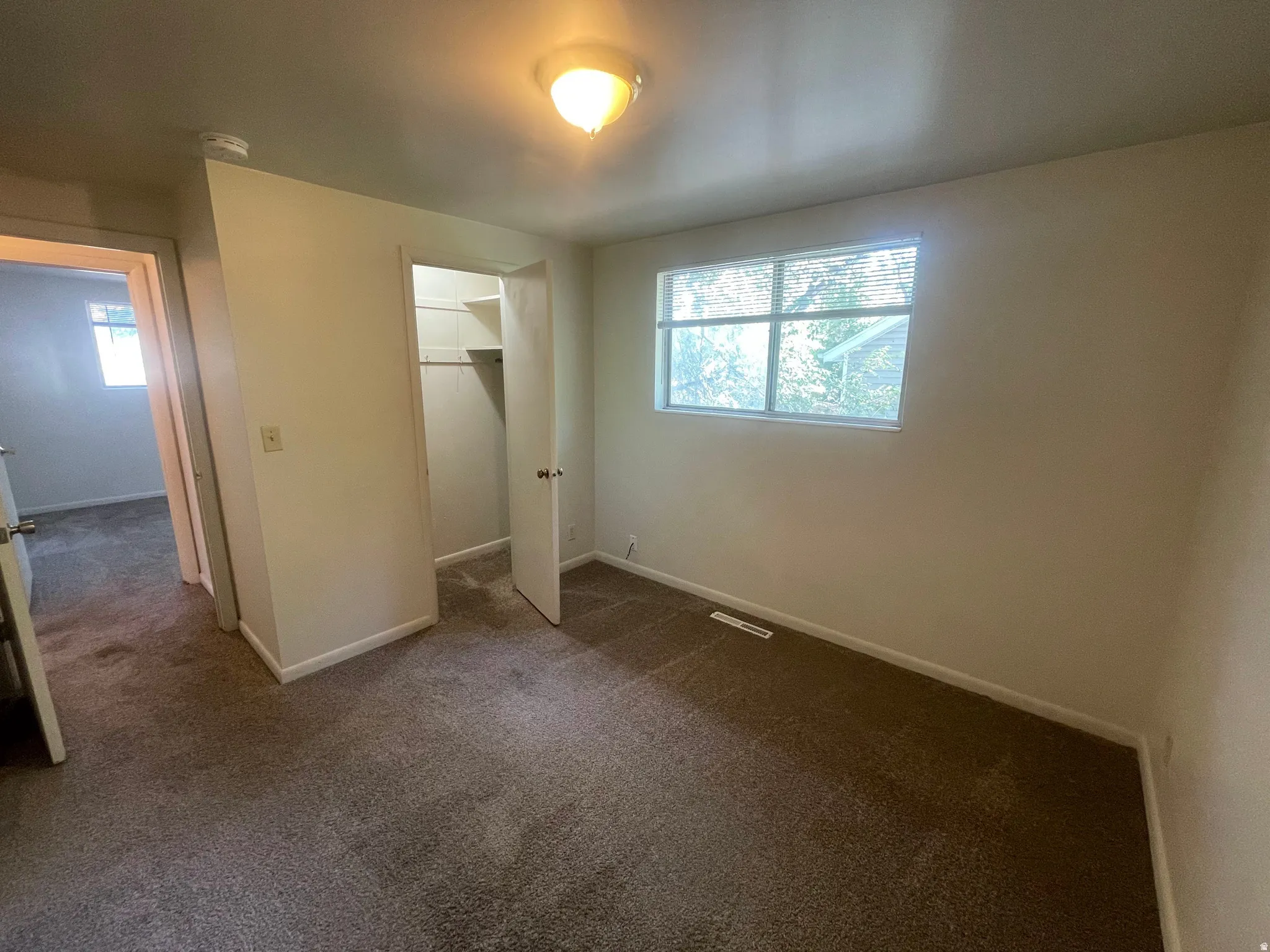 Bedroom featuring neutral carpeting, a double-hung window with blinds, and an open closet with shelving and a hanging rod