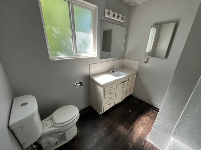 Bathroom featuring a white vanity with integrated sink, a rectangular mirror, and wood-finish flooring