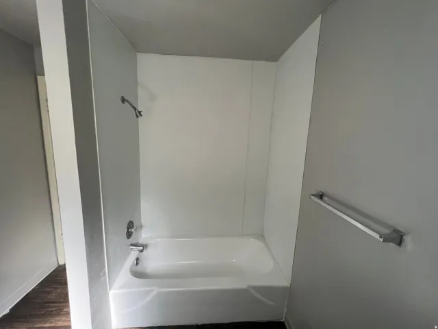 White bathtub and shower surround with chrome fixtures, set against light gray walls