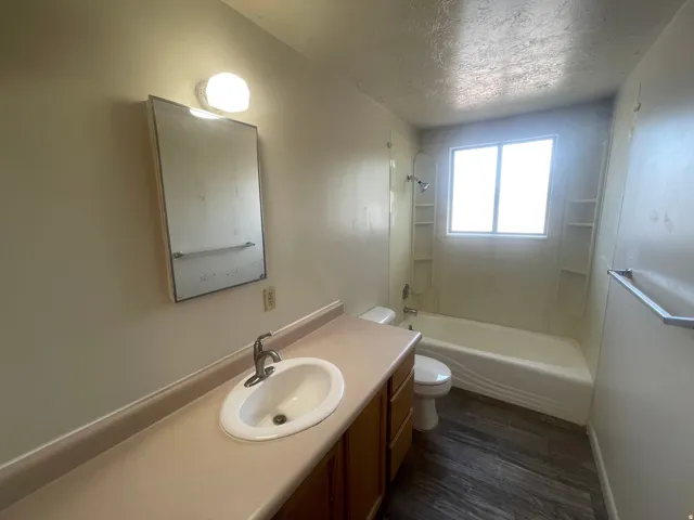 Bathroom featuring a vanity with an integrated sink, a mirror with overhead lighting, a toilet, and a bathtub with a shower and built-in shelving