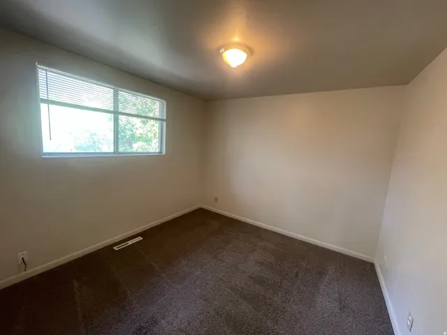 Spacious room featuring neutral wall tones and dark carpeting