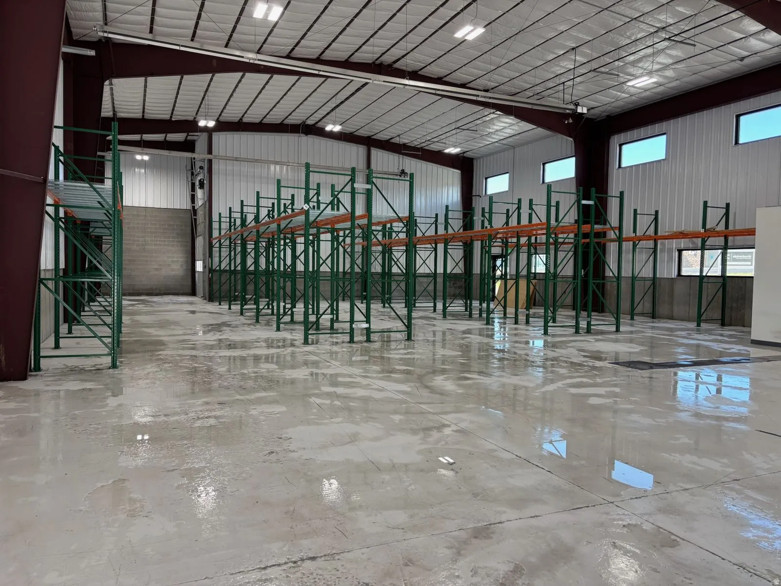 Warehouse interior featuring high ceilings, exposed metal beams, multiple rows of industrial racking, concrete flooring, and ample natural light from upper-level windows