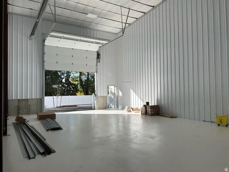 Expansive interior space featuring a large roll-up door, polished concrete flooring, corrugated metal walls, and a visible ceiling structure