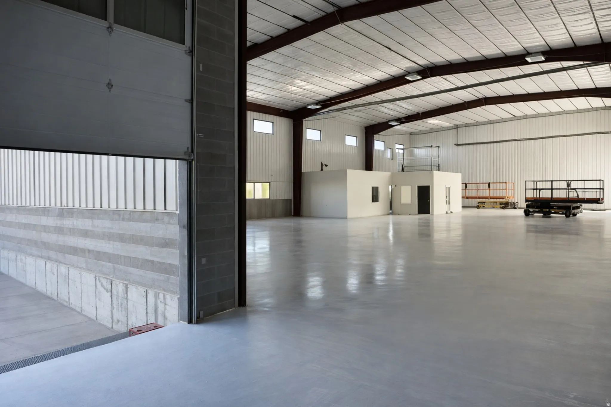 Spacious industrial interior featuring a large roll-up door, polished concrete flooring, exposed steel beams, and high ceilings with fluorescent lighting