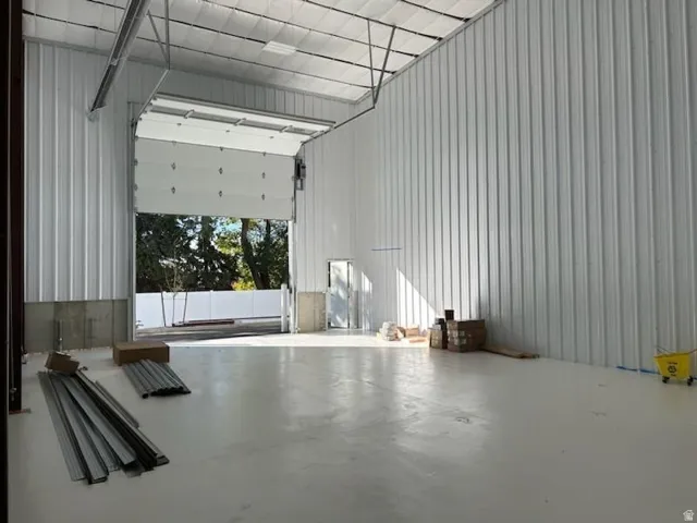 Expansive interior space featuring a large roll-up door, polished concrete flooring, corrugated metal walls, and a visible ceiling structure