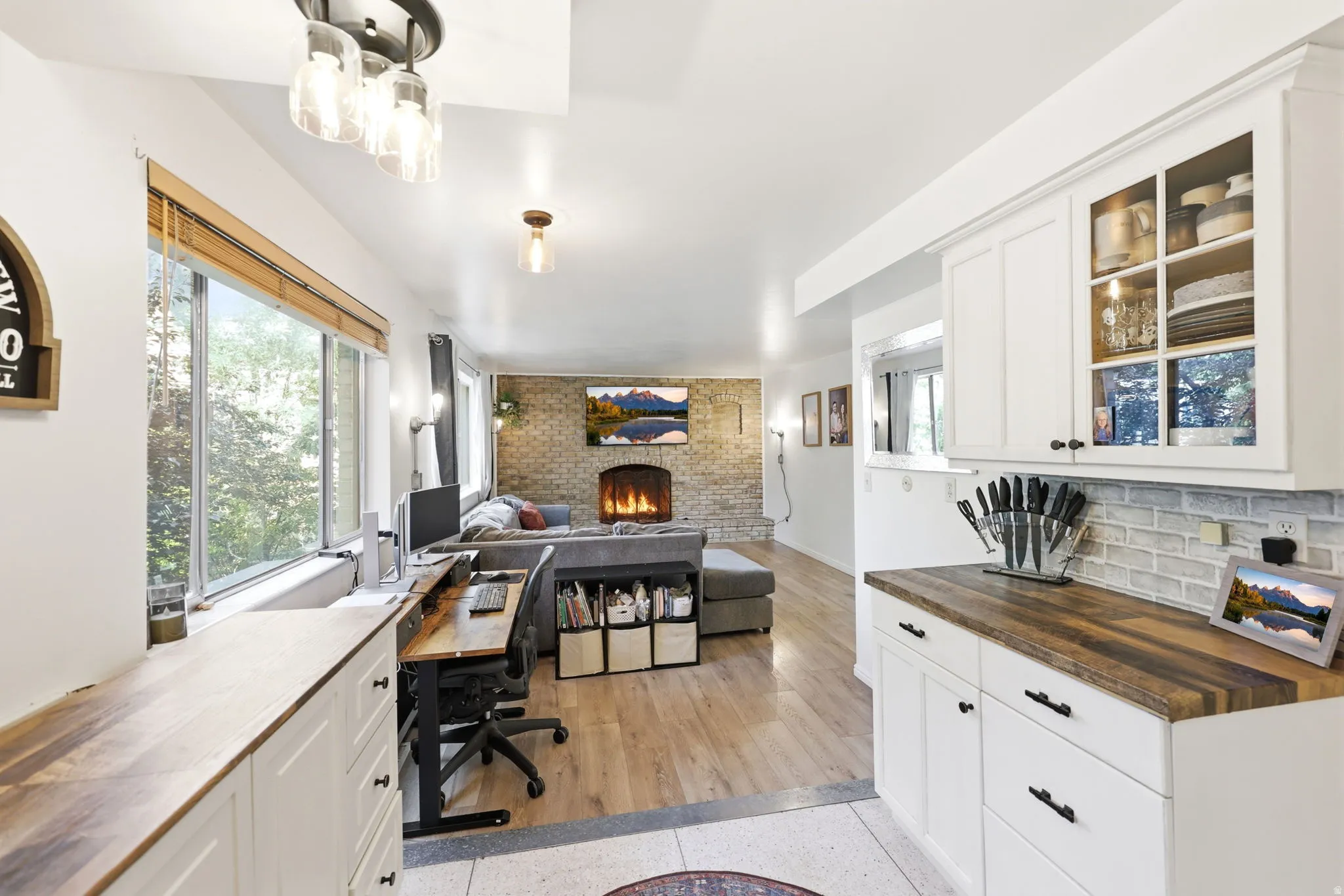 Open concept living area featuring a prominent brick fireplace, wood-finish flooring, and white cabinetry