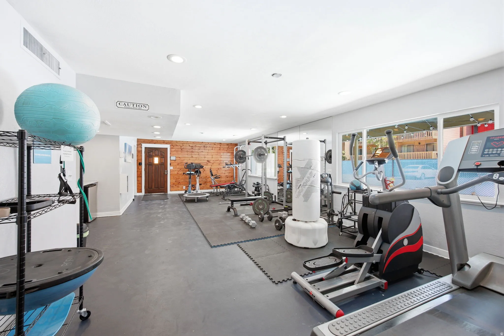 Spacious interior room featuring durable rubber flooring, recessed lighting, a wood accent wall, and multiple windows providing natural illumination