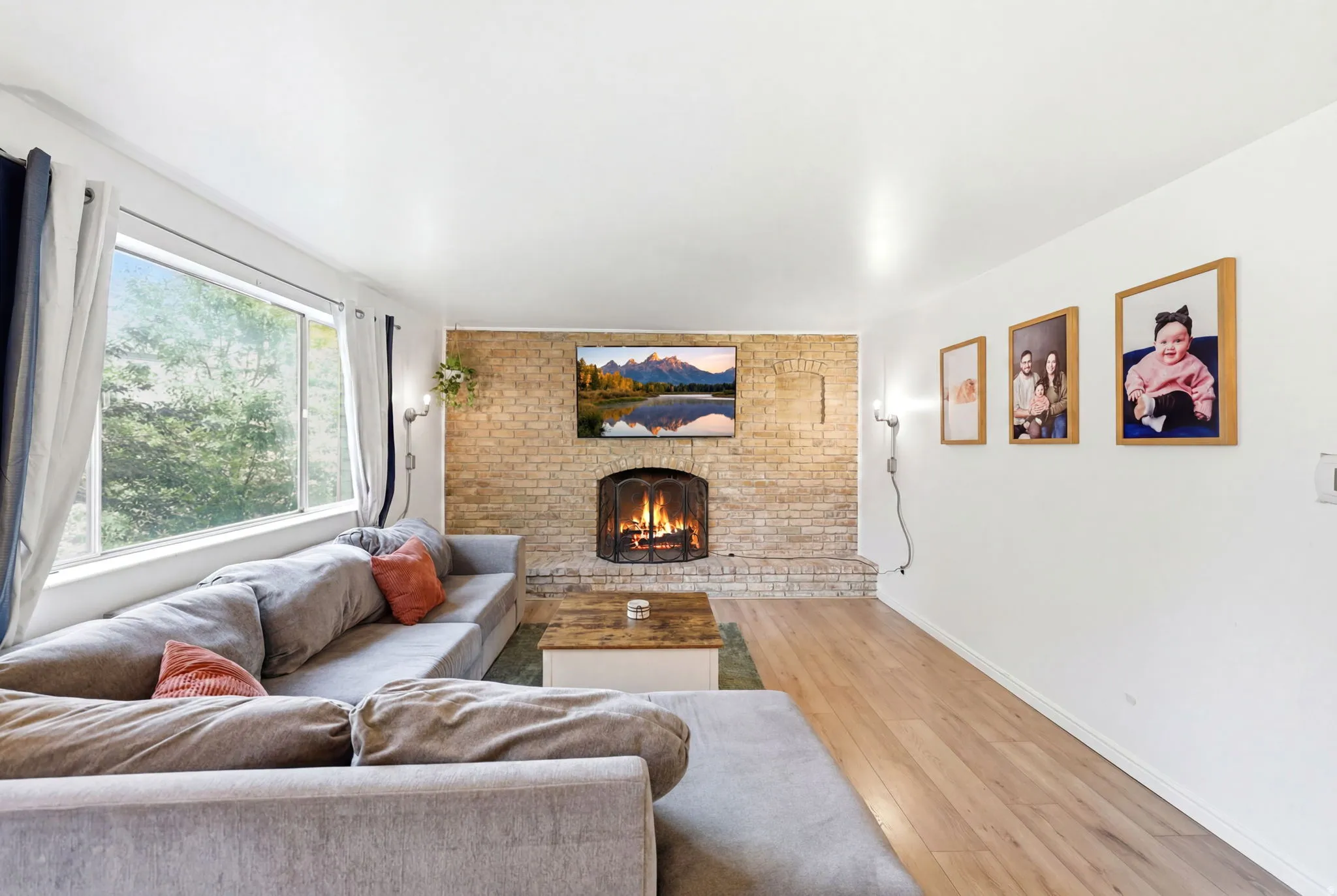 Living area featuring a brick-faced fireplace with a metal screen, wood-finish flooring, and large picture windows