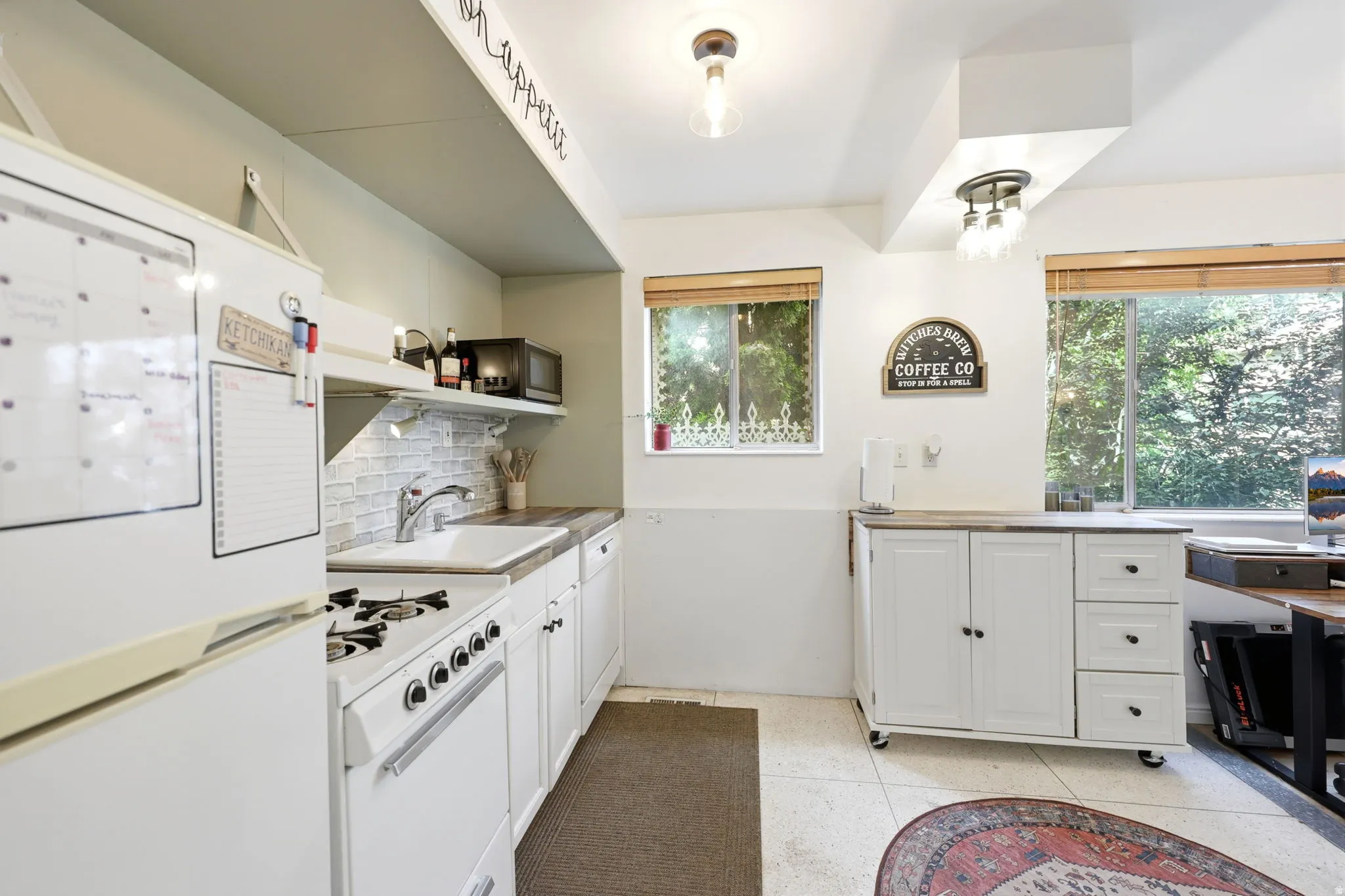 Well-appointed kitchen featuring a white appliance suite, light-colored tile backsplash, and wood-finish countertops