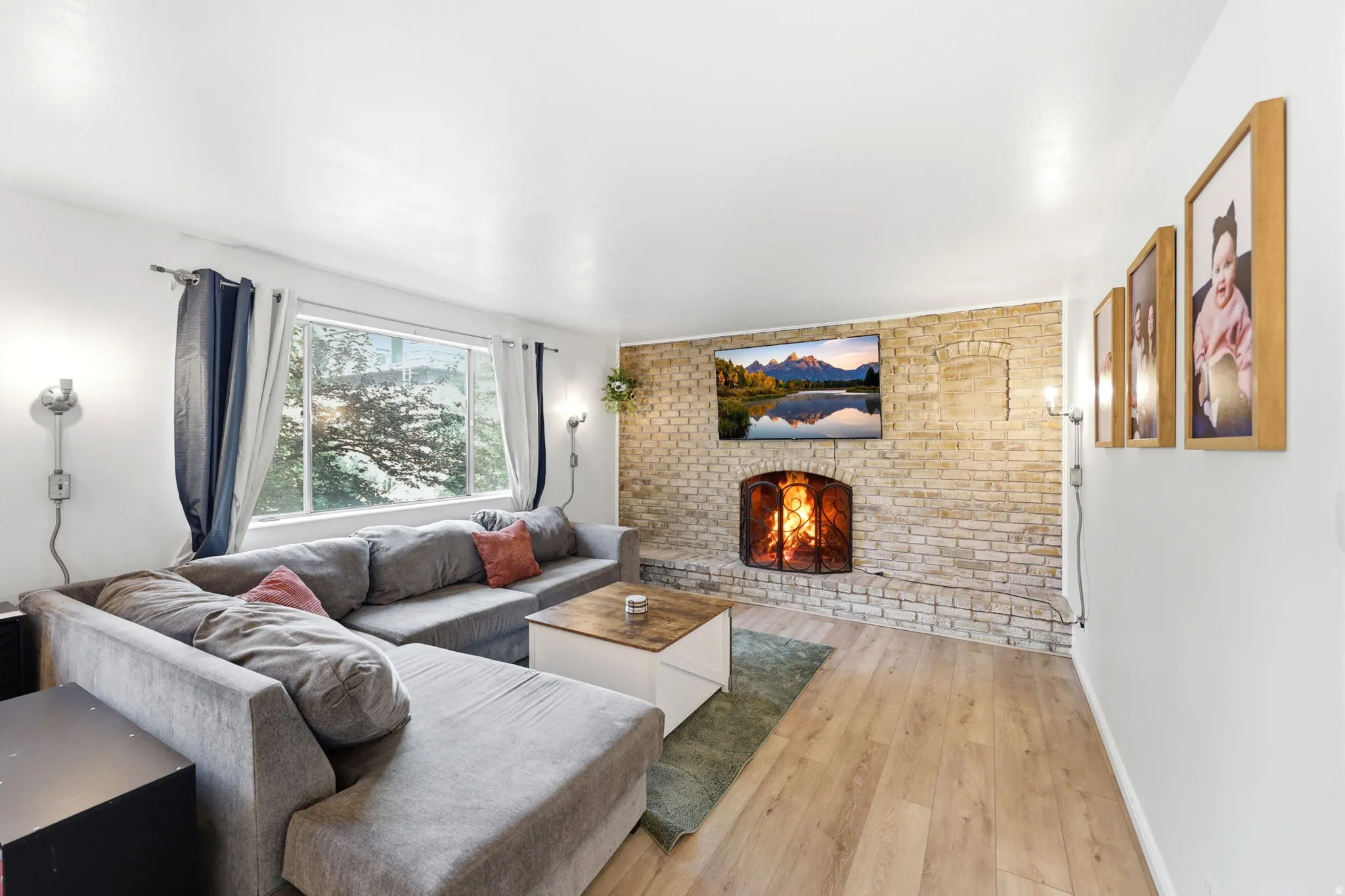 Living area featuring a brick accent wall with a fireplace, wood-finish flooring, and a large window