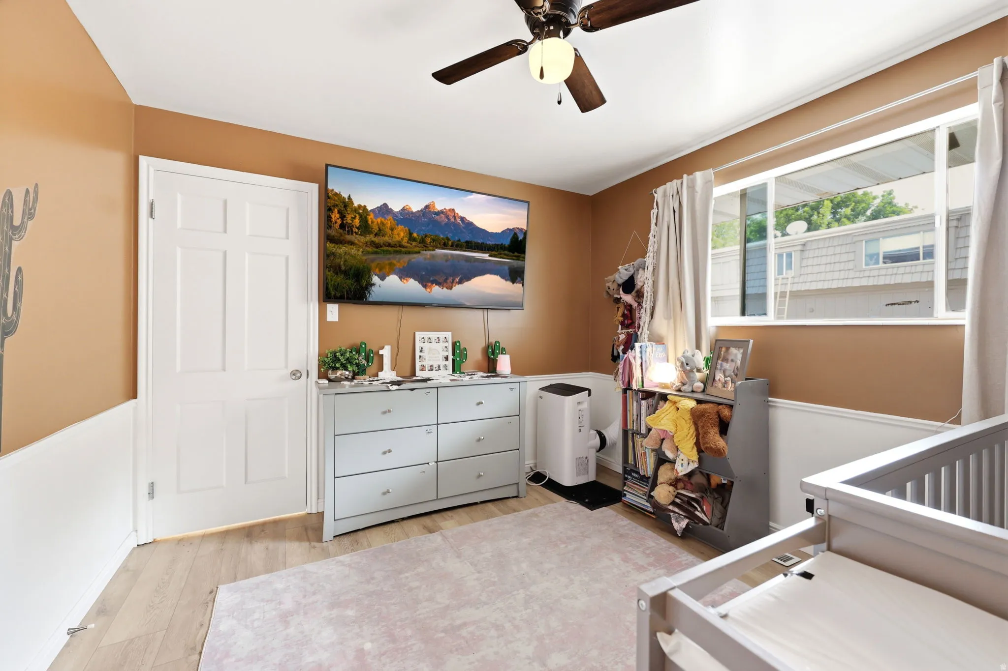 Room featuring wood-finish flooring, a ceiling fan with integrated lighting, and a window with white trim