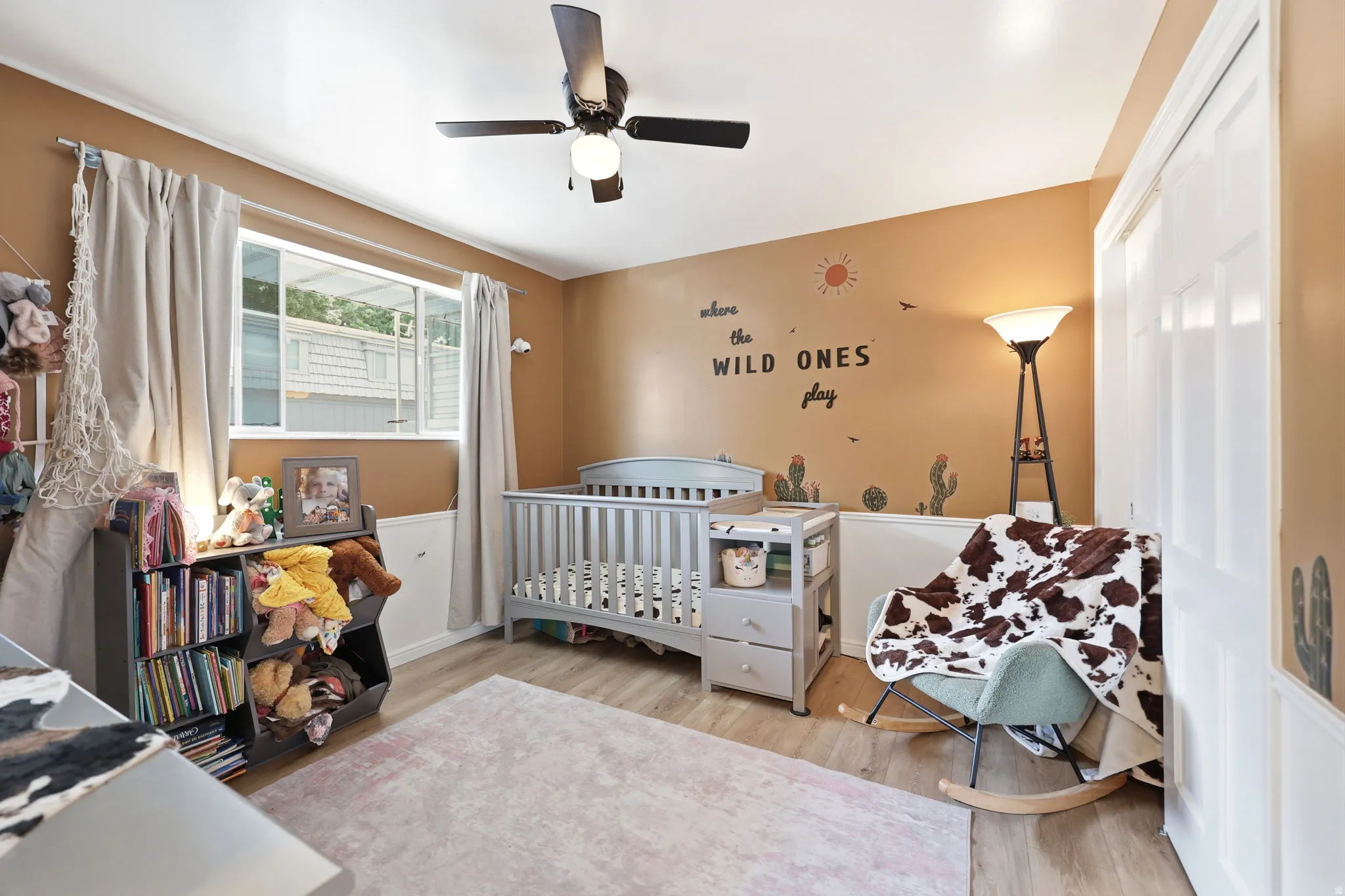 Room featuring a ceiling fan with integrated lighting, wood-finish flooring, a window with curtains, and a two-panel closet door
