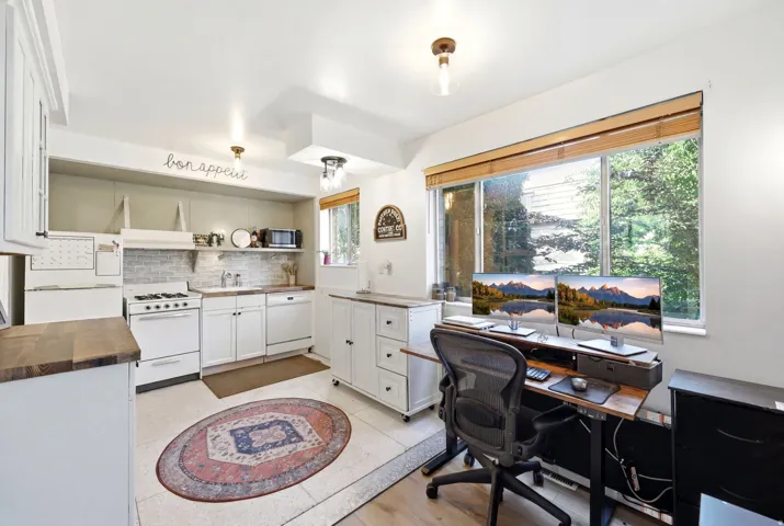 Integrated kitchen and office space featuring white cabinetry and appliances