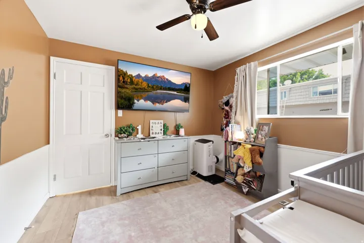 Room featuring wood-finish flooring, a ceiling fan with integrated lighting, and a window with white trim