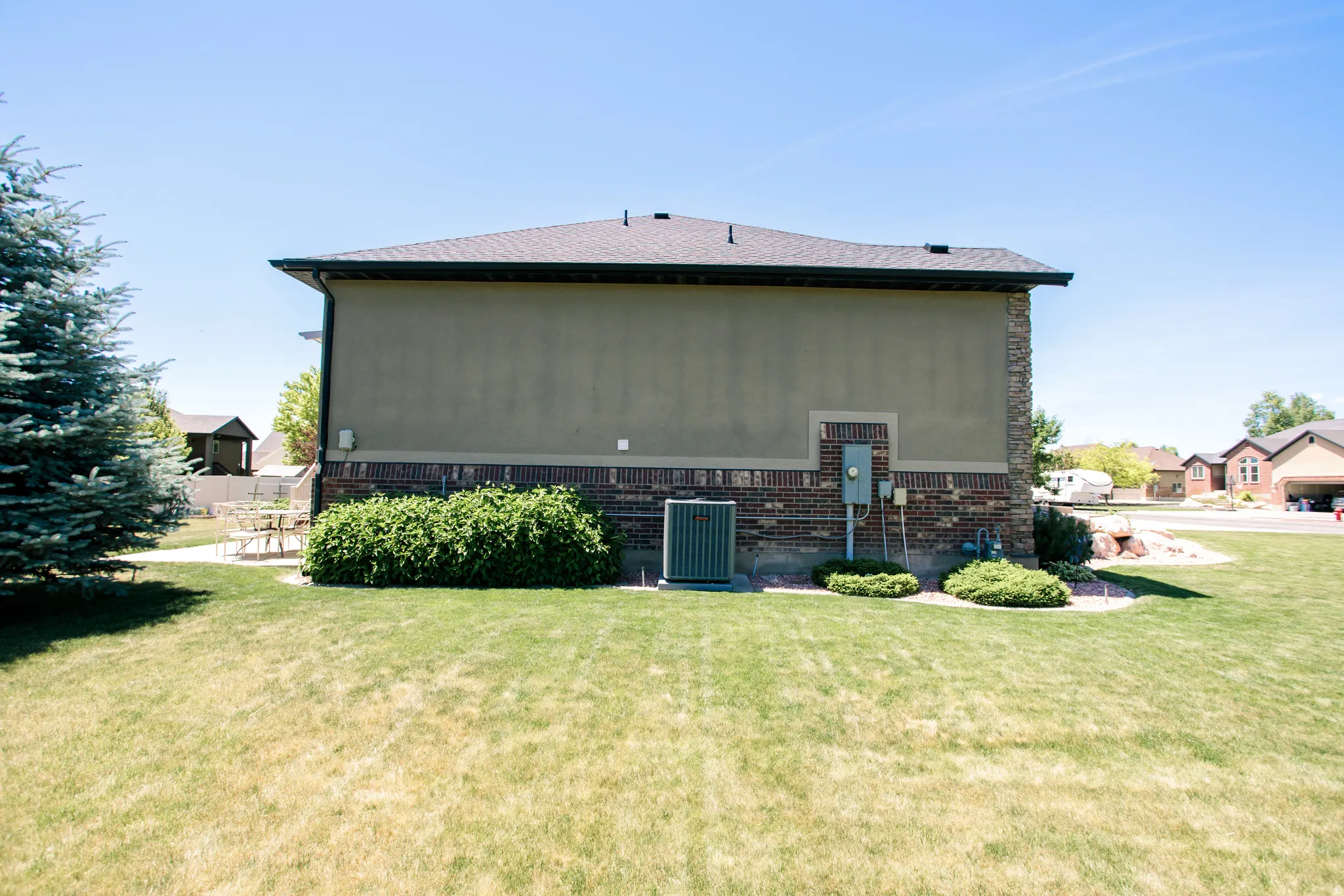 Rear exterior featuring stucco and brick veneer siding, a dark shingle roof, and a mature evergreen tree