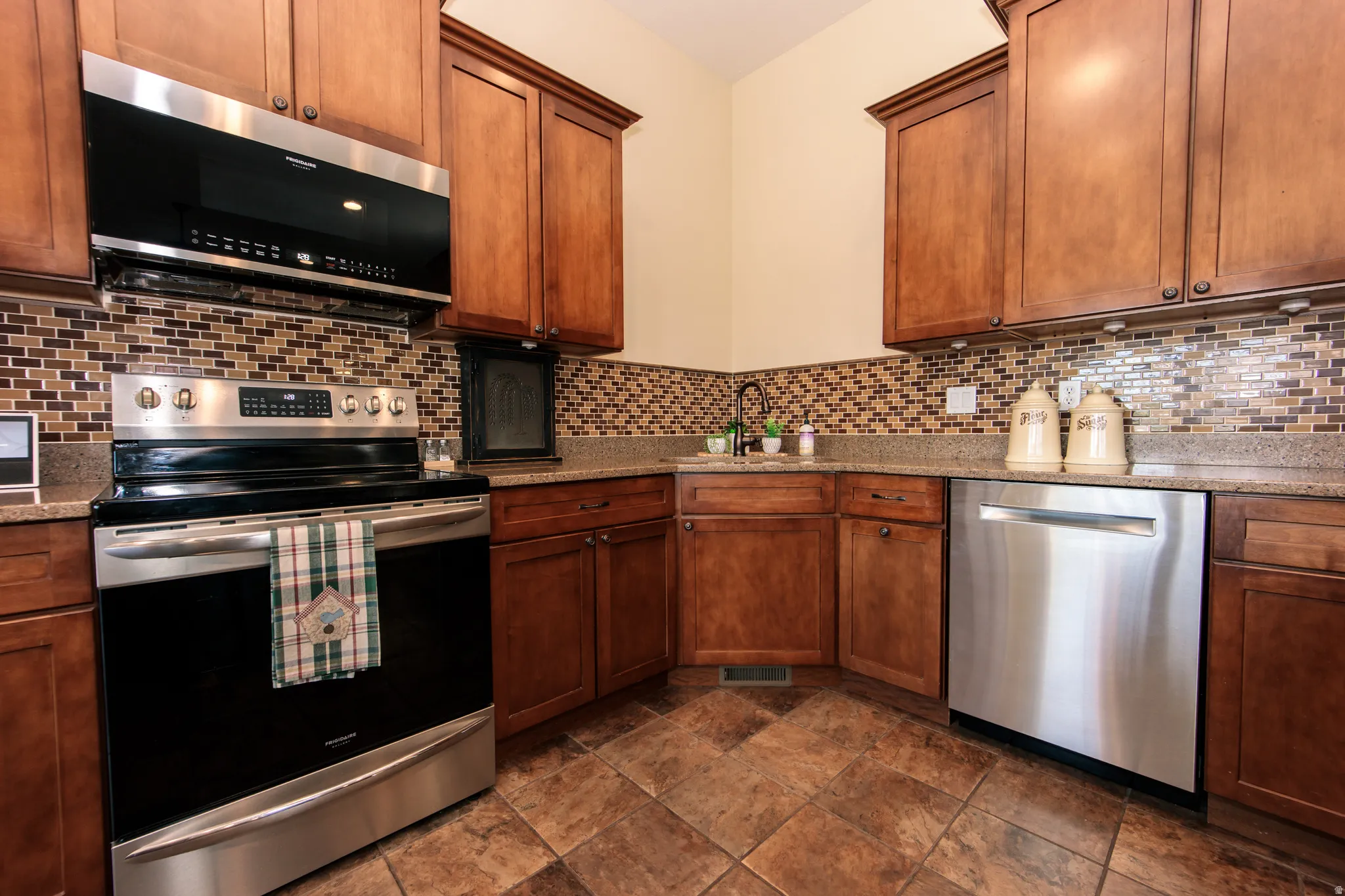 Kitchen featuring wood cabinetry, stainless steel appliances, mosaic tile backsplash, and stone-finish countertops