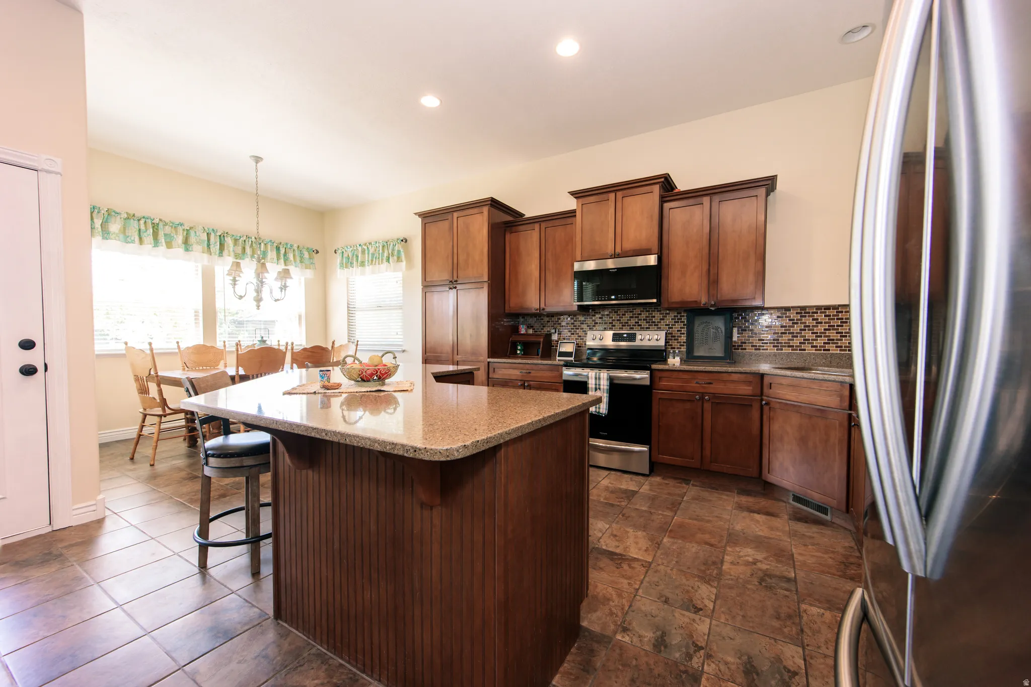 Kitchen featuring wood cabinetry, stainless steel appliances, a patterned tile backsplash, and a central island with a stone-finish countertop