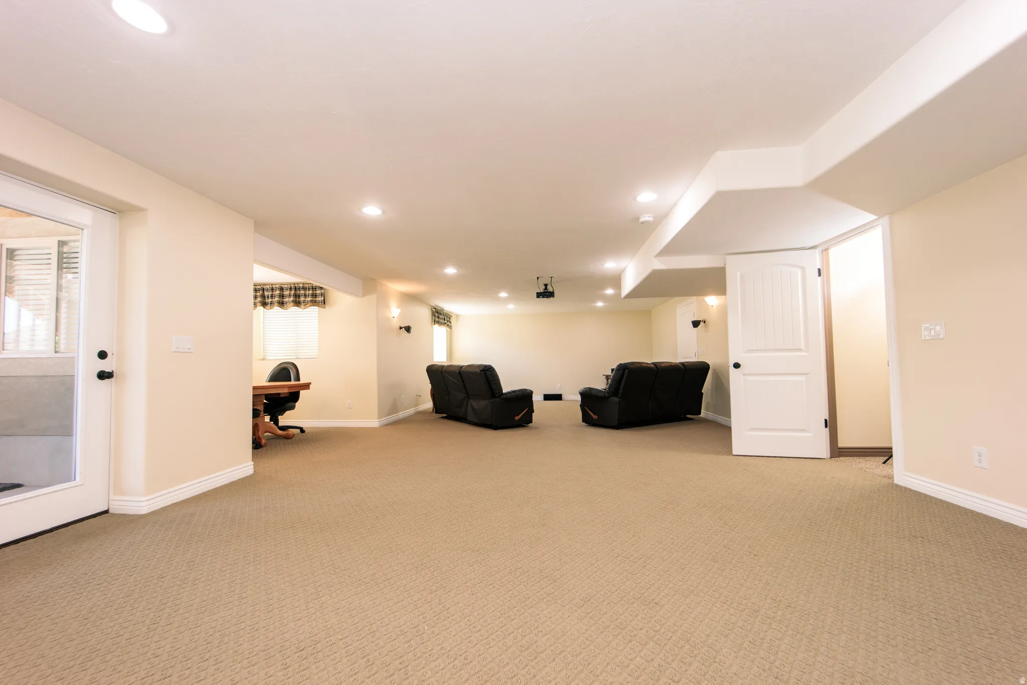 Spacious carpeted room featuring recessed lighting, a built-in projector, a light-colored accent wall, white trim, and a white interior door