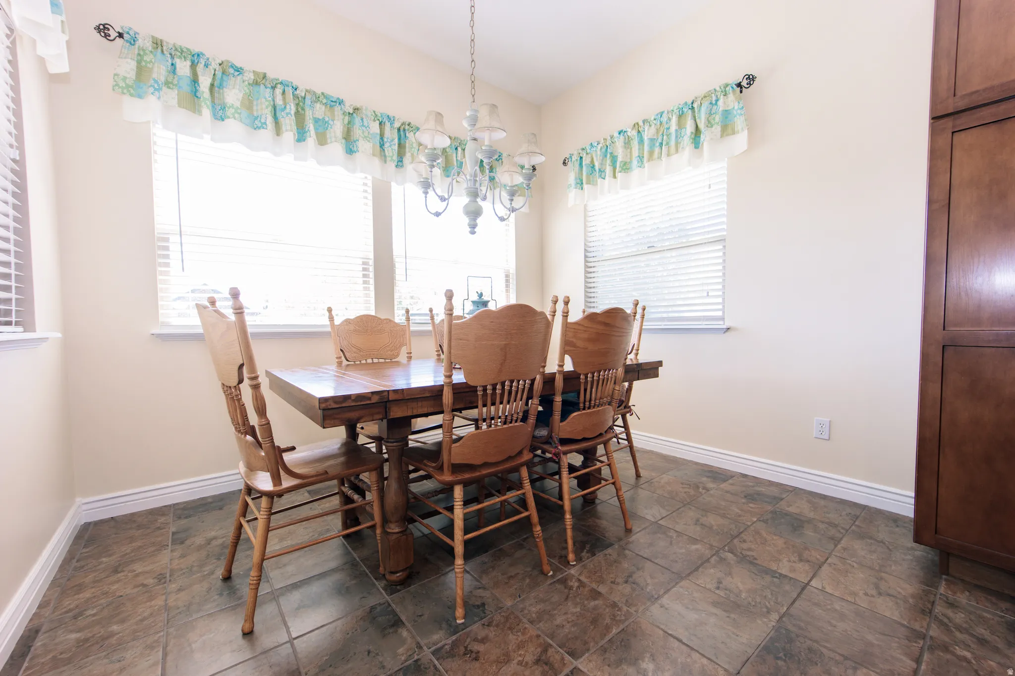 Spacious dining area featuring large windows with blinds, a multi-light chandelier, and durable tile flooring