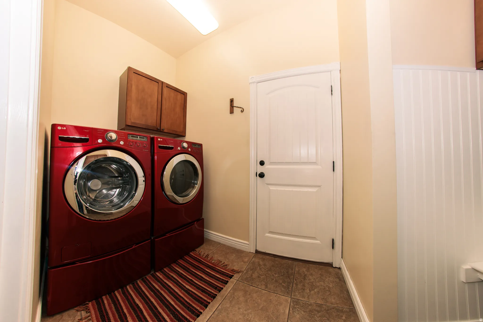 Laundry area featuring tile flooring, a wood-finish wall cabinet, and beadboard wainscoting