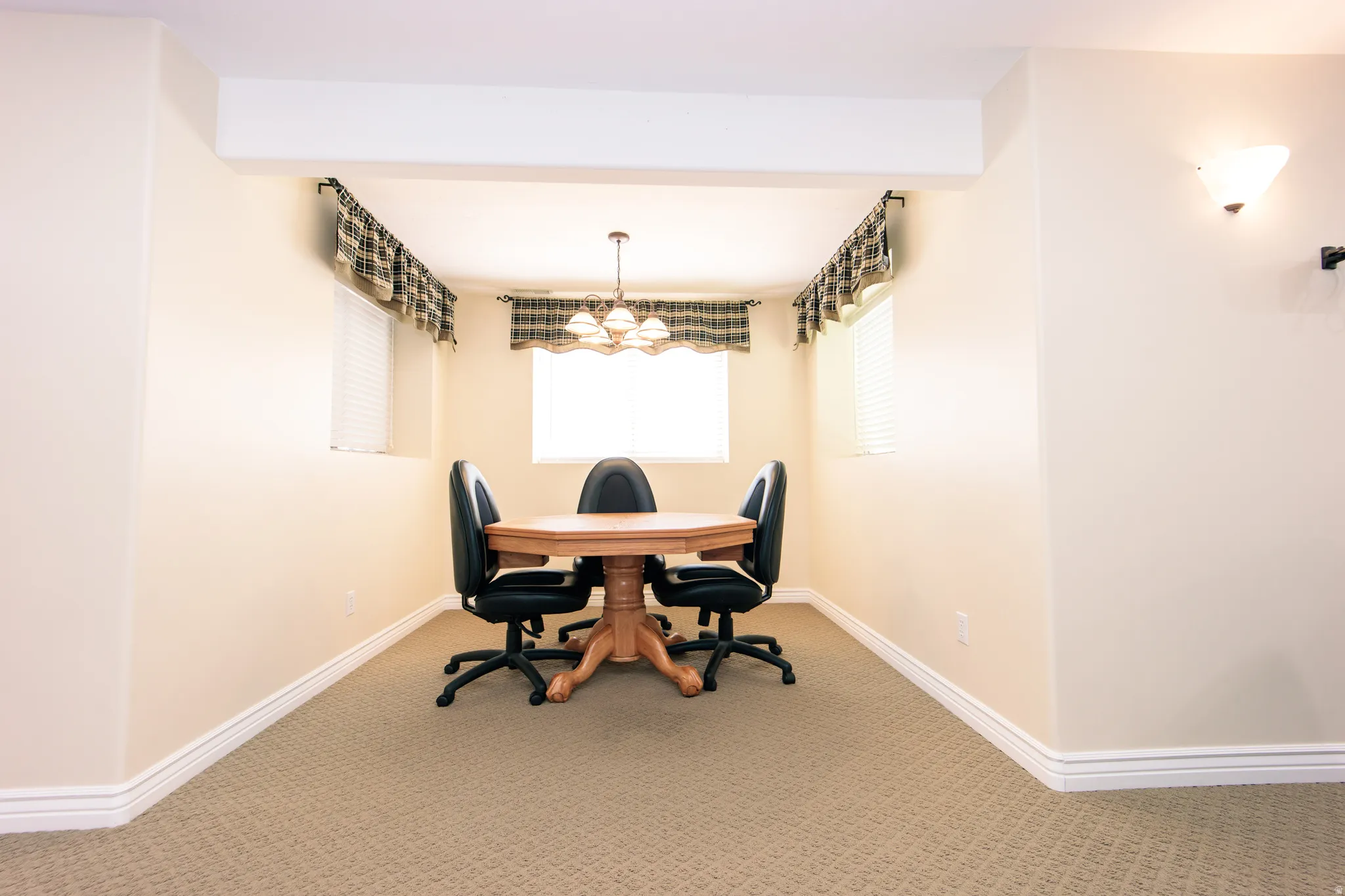 Carpeted area featuring two windows with blinds and valances, illuminated by a central chandelier and a wall sconce