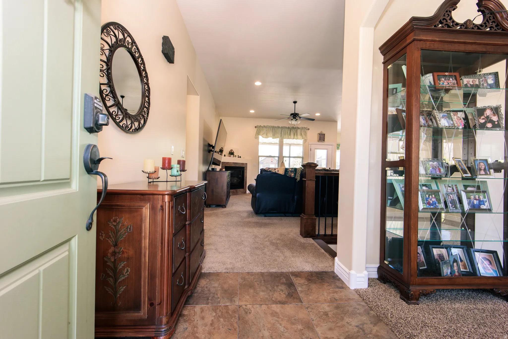 Entryway with tile flooring opening to a carpeted living space featuring a fireplace, a ceiling fan, and a light-colored main door