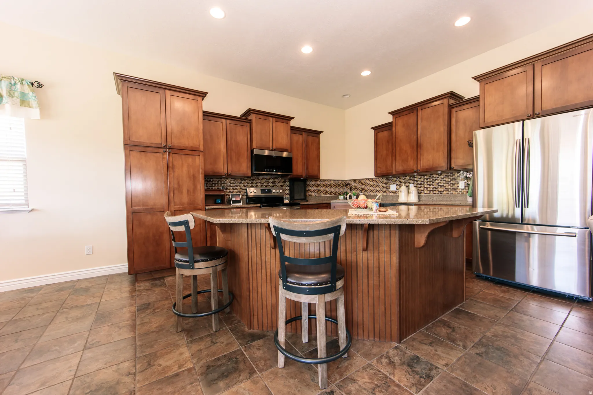 Kitchen featuring a central island with countertop seating, rich wood-finish cabinetry, stainless steel appliances, and tile flooring