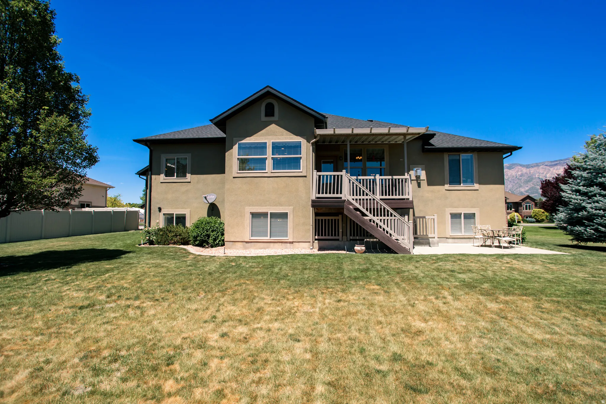 Rear exterior featuring a multi-level deck, ground-level patio, mature landscaping, and stucco siding