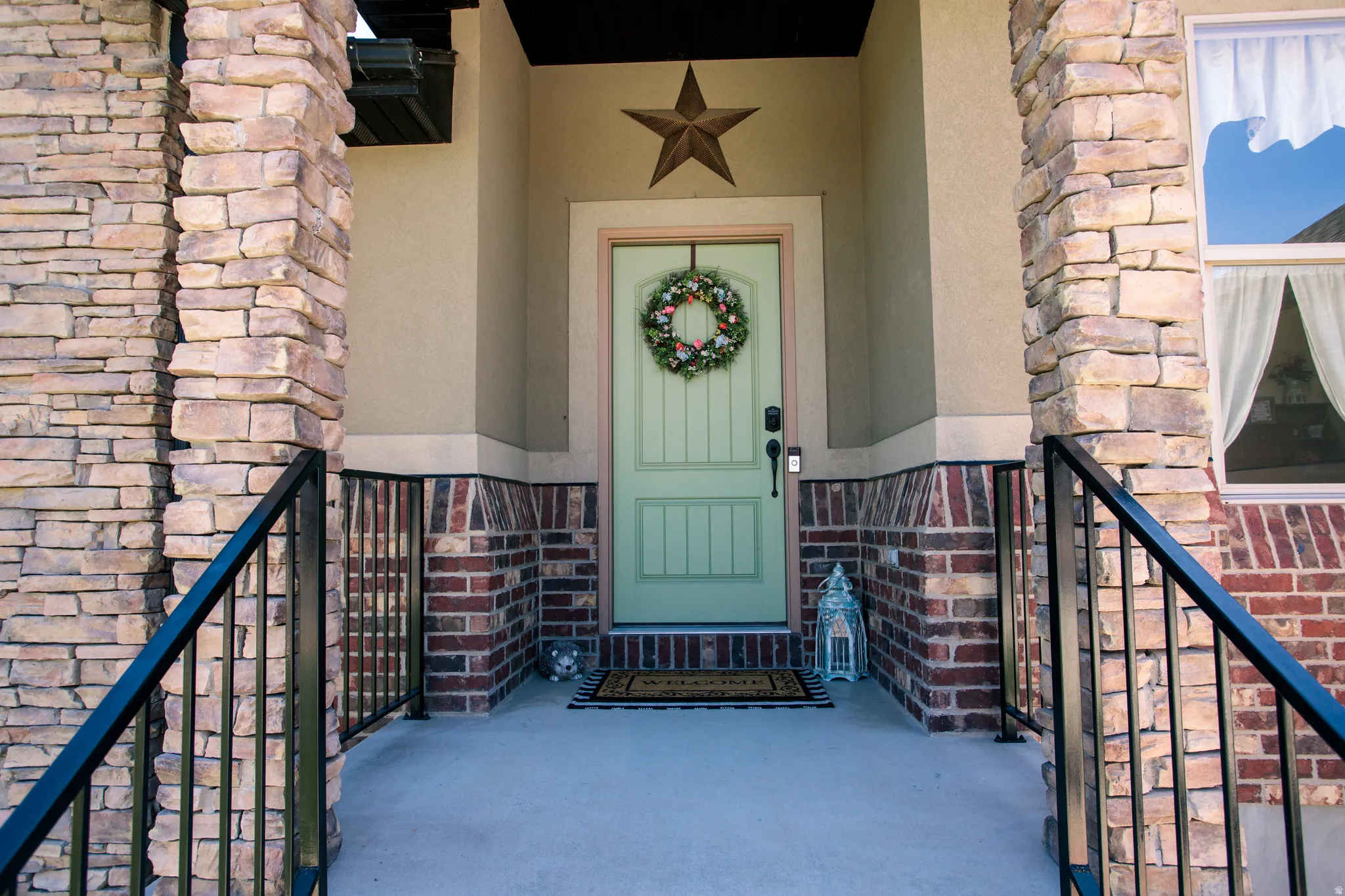 Front entry featuring a light green door, stone facade, brick detailing, black metal railings, and concrete steps