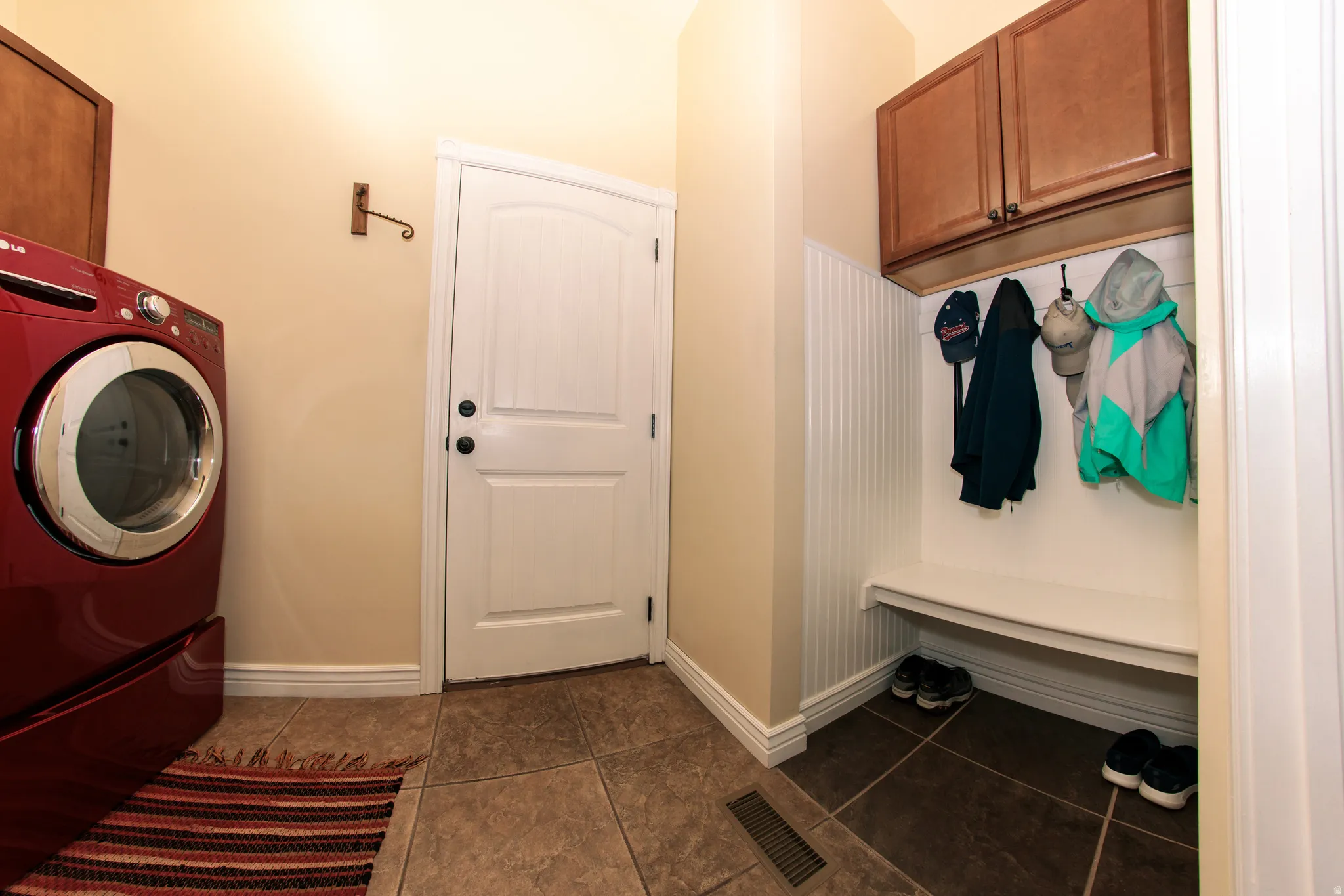 Functional mudroom featuring a built-in bench, upper cabinetry, beadboard paneling, and ceramic tile flooring