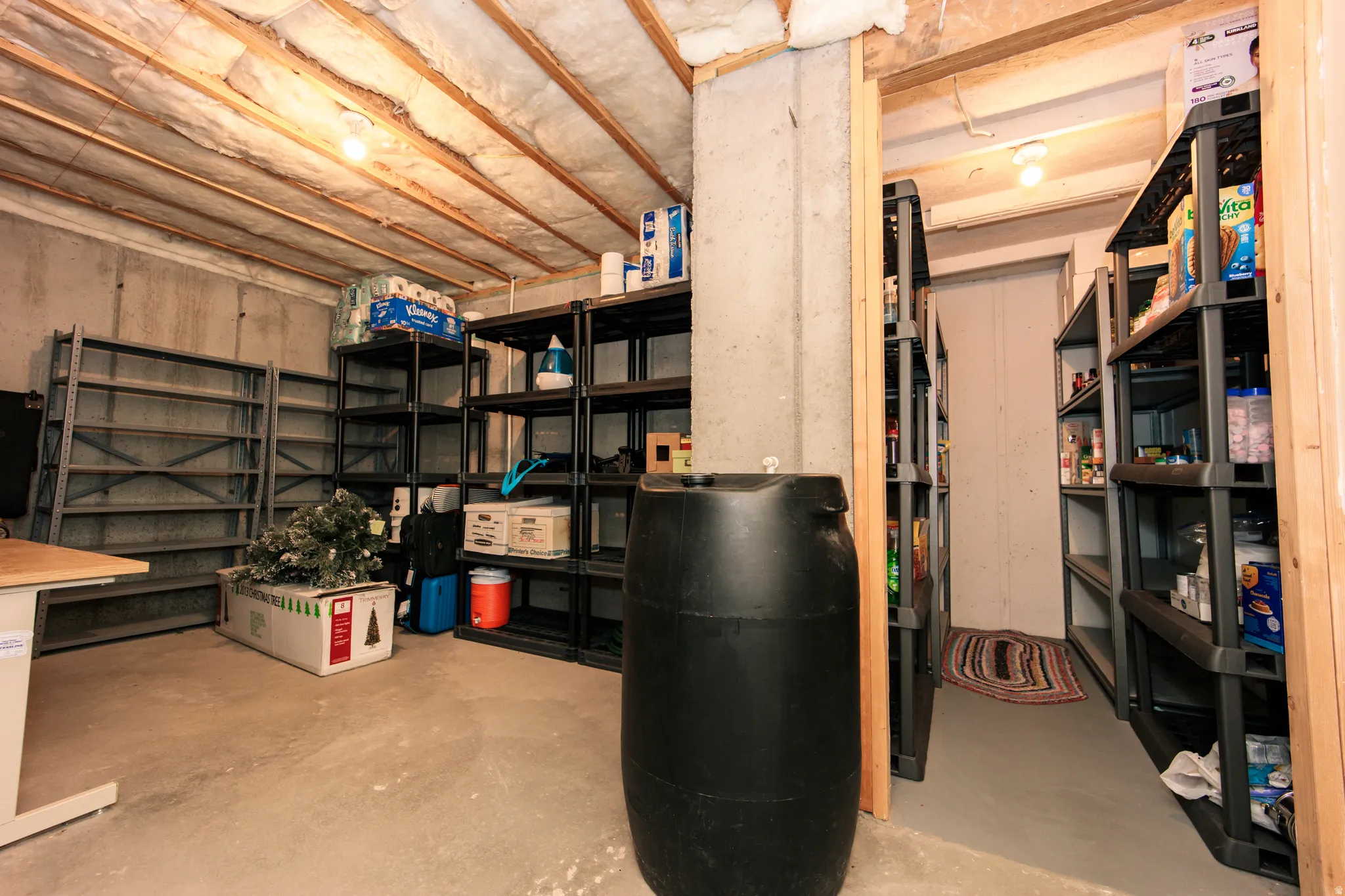 Unfinished basement space featuring exposed wood joists, concrete walls, concrete flooring, and an open doorway