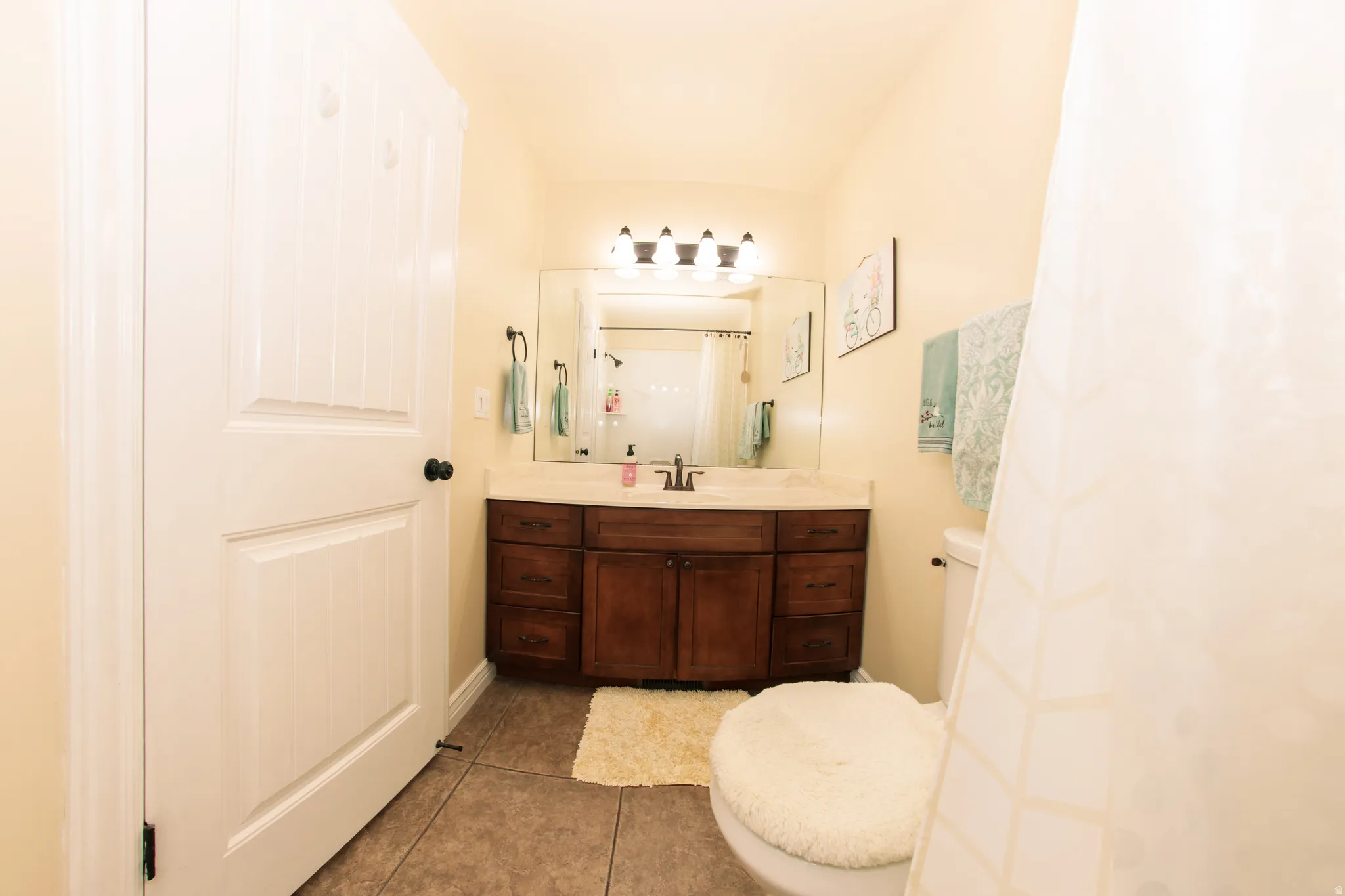 Bathroom featuring a wood-finish vanity with a light-toned countertop, a rectangular mirror, and a four-light fixture