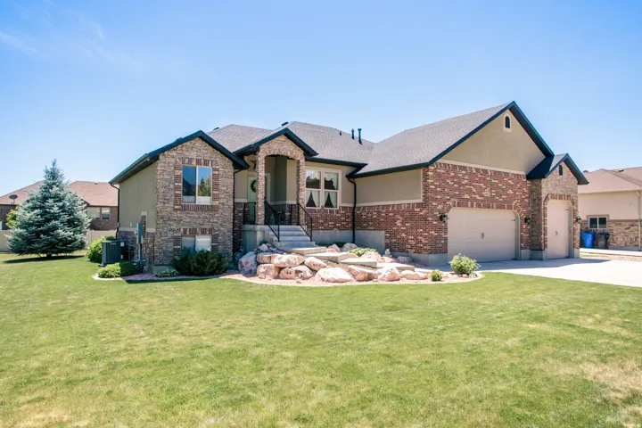Stucco and brick facade residence featuring an arched portico entry with black railing, multiple gable roofs, and a dual garage with carriage-style doors