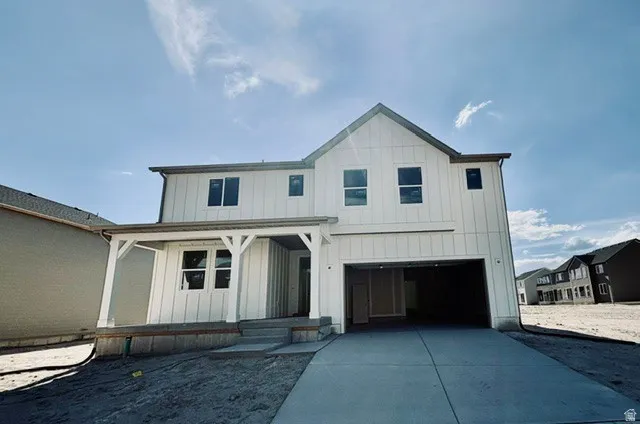 Modern farmhouse-style exterior featuring vertical board and batten siding, a covered front porch with white pillars, a two-car garage, and a concrete driveway