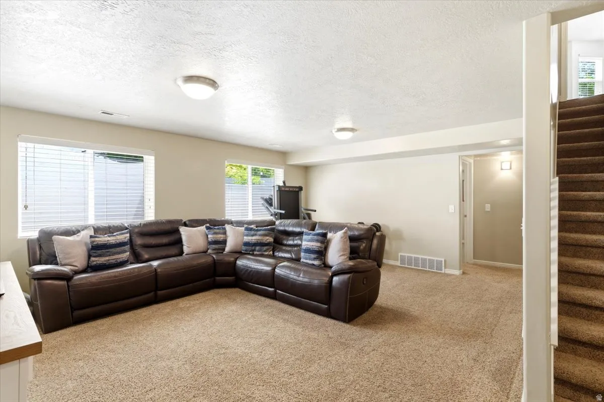 Carpeted recreation room featuring natural light from multiple windows, recessed ceiling lighting, and a carpeted staircase