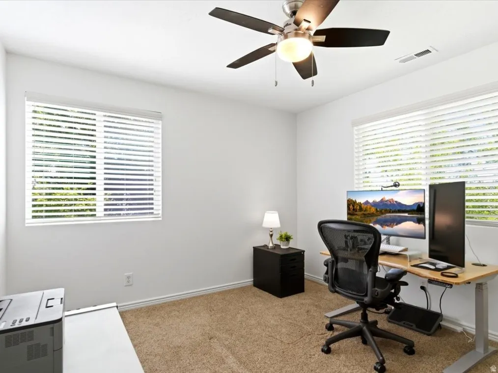 Carpeted room with a ceiling fan light fixture, two windows with blinds, white painted walls, and white trim
