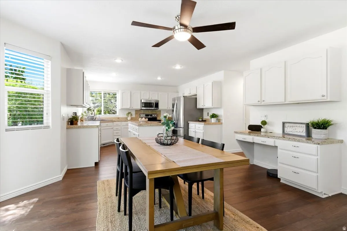 Open-concept kitchen and dining area featuring wood-finish flooring, white cabinetry, recessed lighting, stainless steel appliances, and a built-in desk area with overhead storage