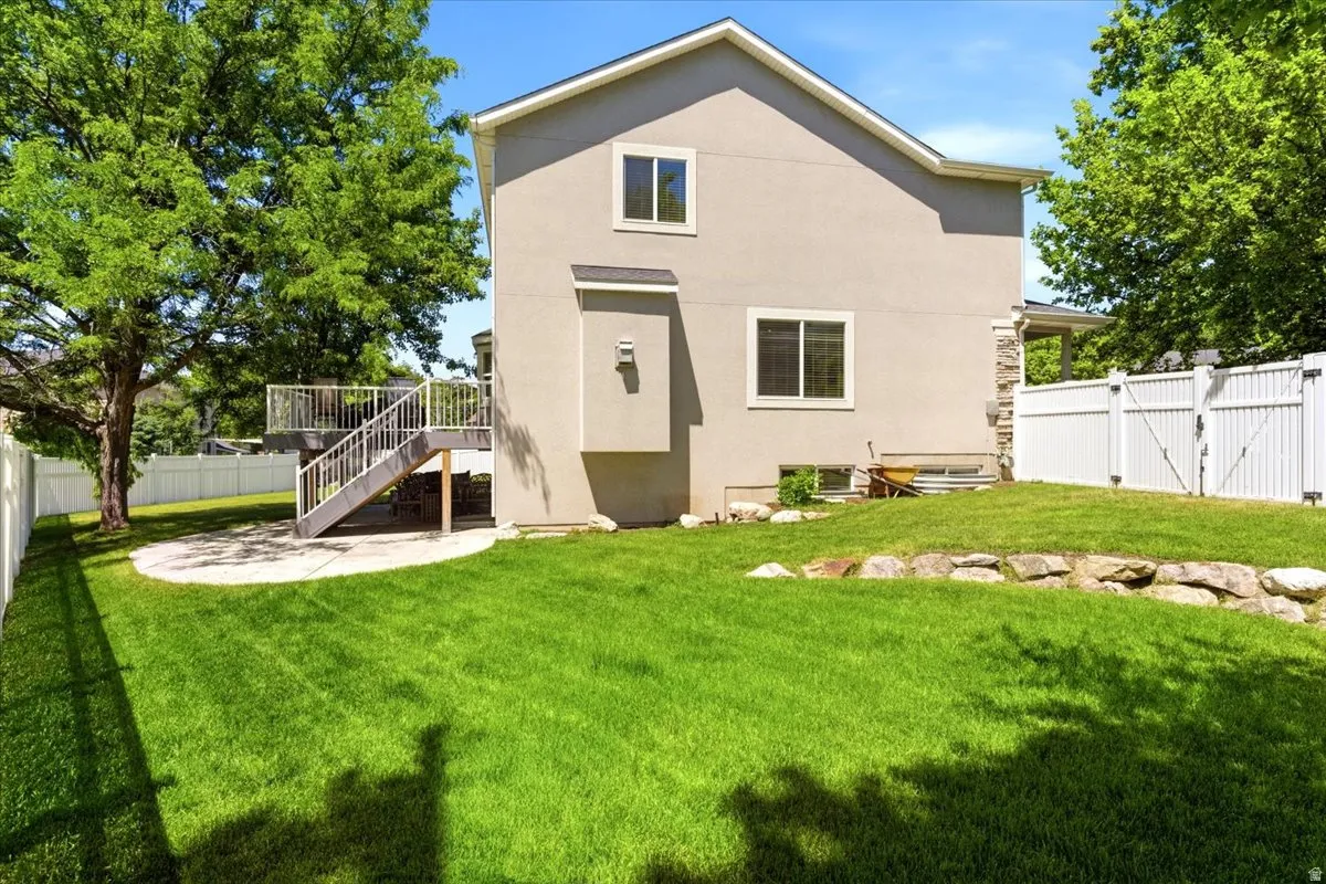 Expansive backyard featuring a lush lawn, concrete patio, and a raised wood-finish deck with white railings