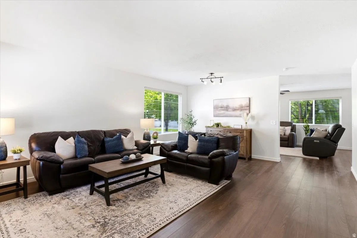 Spacious living area featuring wood-finish flooring, white walls, and multiple windows with blinds
