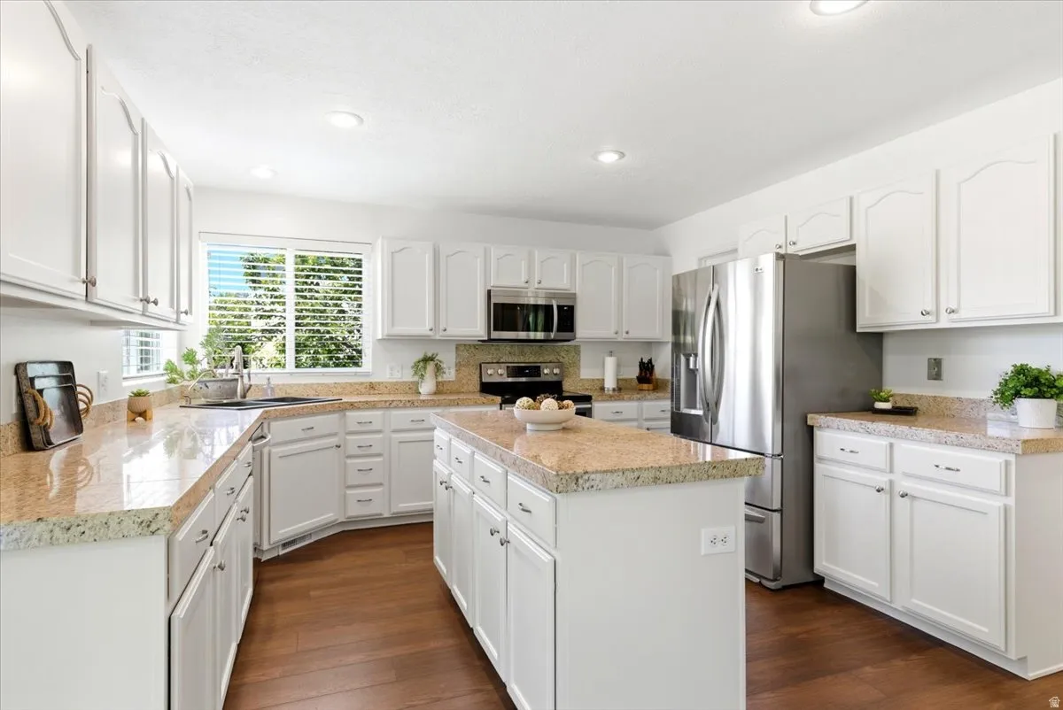 Kitchen featuring white cabinetry, granite countertops, stainless steel appliances, a central island, and wood-finish flooring