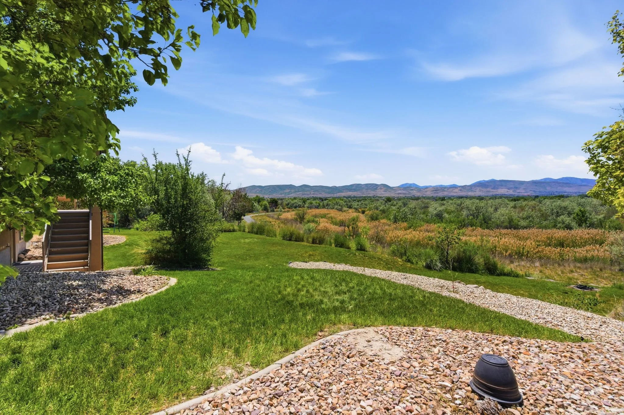 Landscaped grounds featuring a tiered lawn, gravel pathways, mature trees, and natural scenery