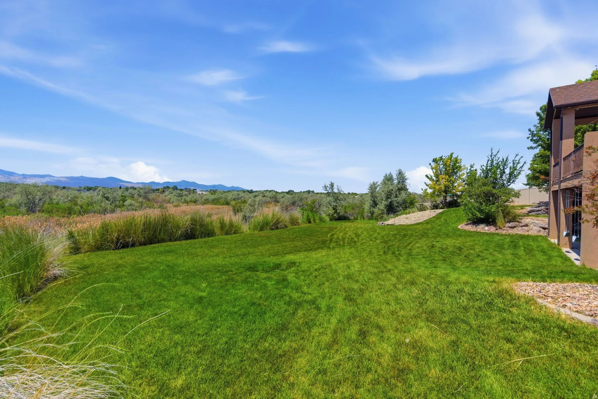 Expansive backyard featuring a manicured lawn, established landscaping, and a broad horizon with distant mountains