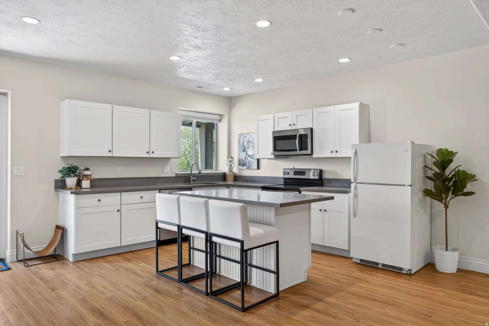 Kitchen featuring white shaker cabinetry, dark countertops, wood-finish flooring, a central island with seating, and recessed lighting