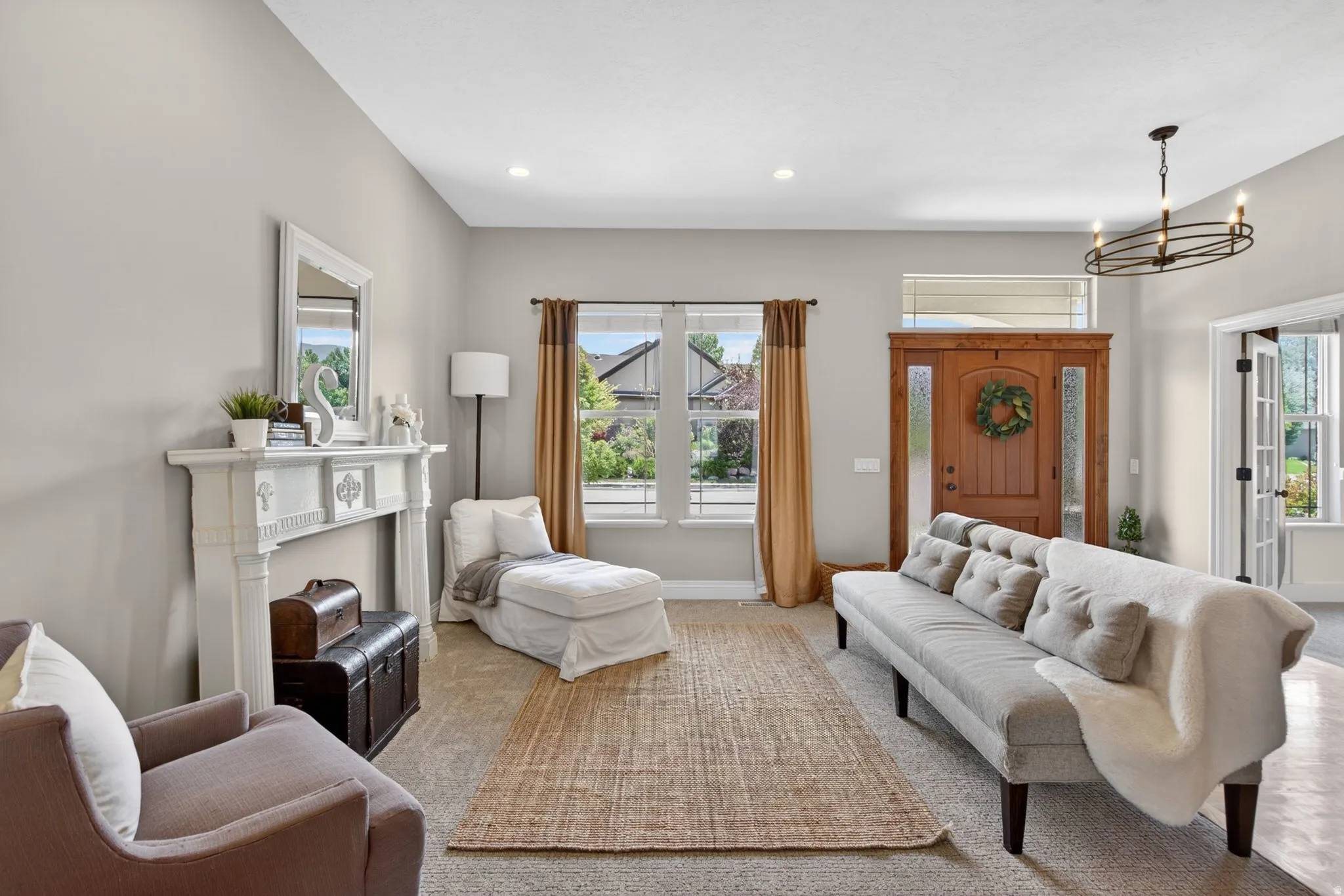 Bright living space featuring a decorative fireplace mantel, wood entry door with sidelights and transom window, and a prominent chandelier