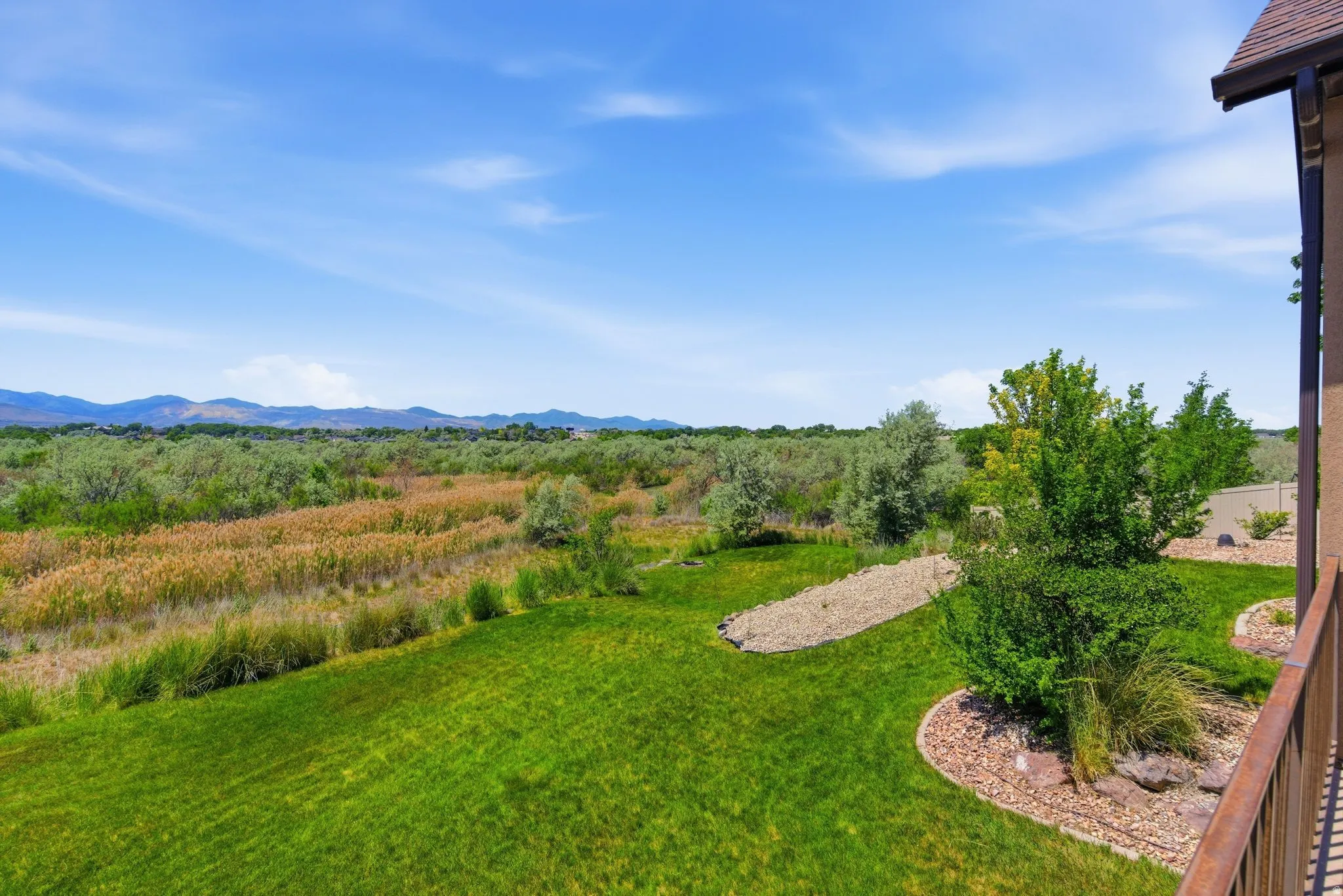 Expansive backyard featuring a manicured lawn, established landscaping, decorative rock beds, and a distant mountain range under a clear blue sky