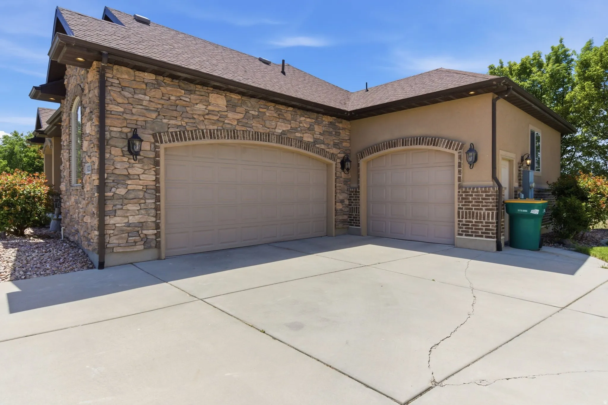 Exterior featuring a two-car garage with arched brick detailing, stone veneer accents, stucco siding, and a concrete driveway
